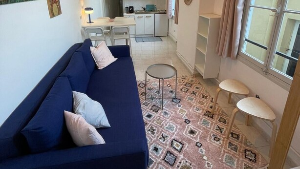 Una sala de estar moderna con un sofá azul, una alfombra estampada y una cocina al fondo.