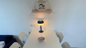Un comedor con una mesa blanca, cuatro sillas, un tazón pequeño, una lámpara y un letrero colgado en la pared.