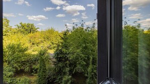 Blick aus einem Fenster auf eine üppige grüne Landschaft mit Bäumen und blauem Himmel.