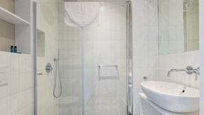 Ein modernes Badezimmer mit einer gläsernen Duschkabine, einem weißen Waschbecken und einem gefliesten Boden.