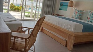 A hotel room with a bed, a desk, and a chair. There is a large window with a view of a pool and palm trees.