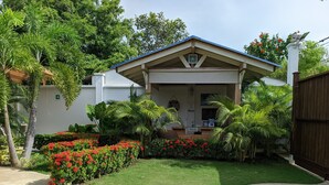 A house with a front porch, a small garden with red flowers, and a wooden fence.