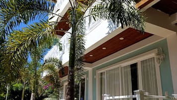 A hotel with a modern design, featuring a balcony with wooden railings, a well-maintained lawn, and tropical plants.