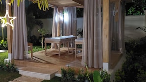 An outdoor seating area with a wooden pergola, covered by curtains, and a star-shaped light fixture.