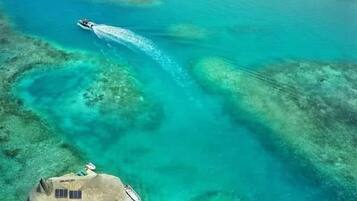 Vista aérea de una isla tropical con aguas turquesas cristalinas, una estructura de techo de paja y varias islas más pequeñas al fondo.
