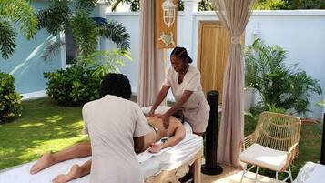 A massage therapy session in a wooden outdoor setting with a pergola, a massage table, and a chair.