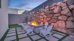 An outdoor patio with a fire feature, white chairs, and a stone wall. - Desert Mirage: Private Pool, Foosball, Putting Green, Wheelchair Access (Hurricane)