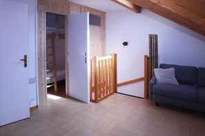 A room with a wooden ceiling, a grey sofa, a white door, and a wooden gate leading to a loft area. - Ski-in/ski-out & foot of the slopes, 2nd floor, swimming pool, sauna, balcony, tv, ski locker, 62m² (Les Orres)