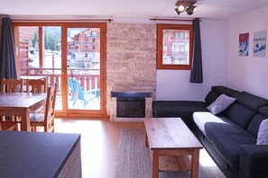 A living room with a stone fireplace, a sofa, a dining table with chairs, and a view of a wooden building through a glass door. - Ski-in/ski-out & foot of the slopes, 2nd floor, swimming pool, sauna, balcony, tv, ski locker, 62m² (Les Orres)