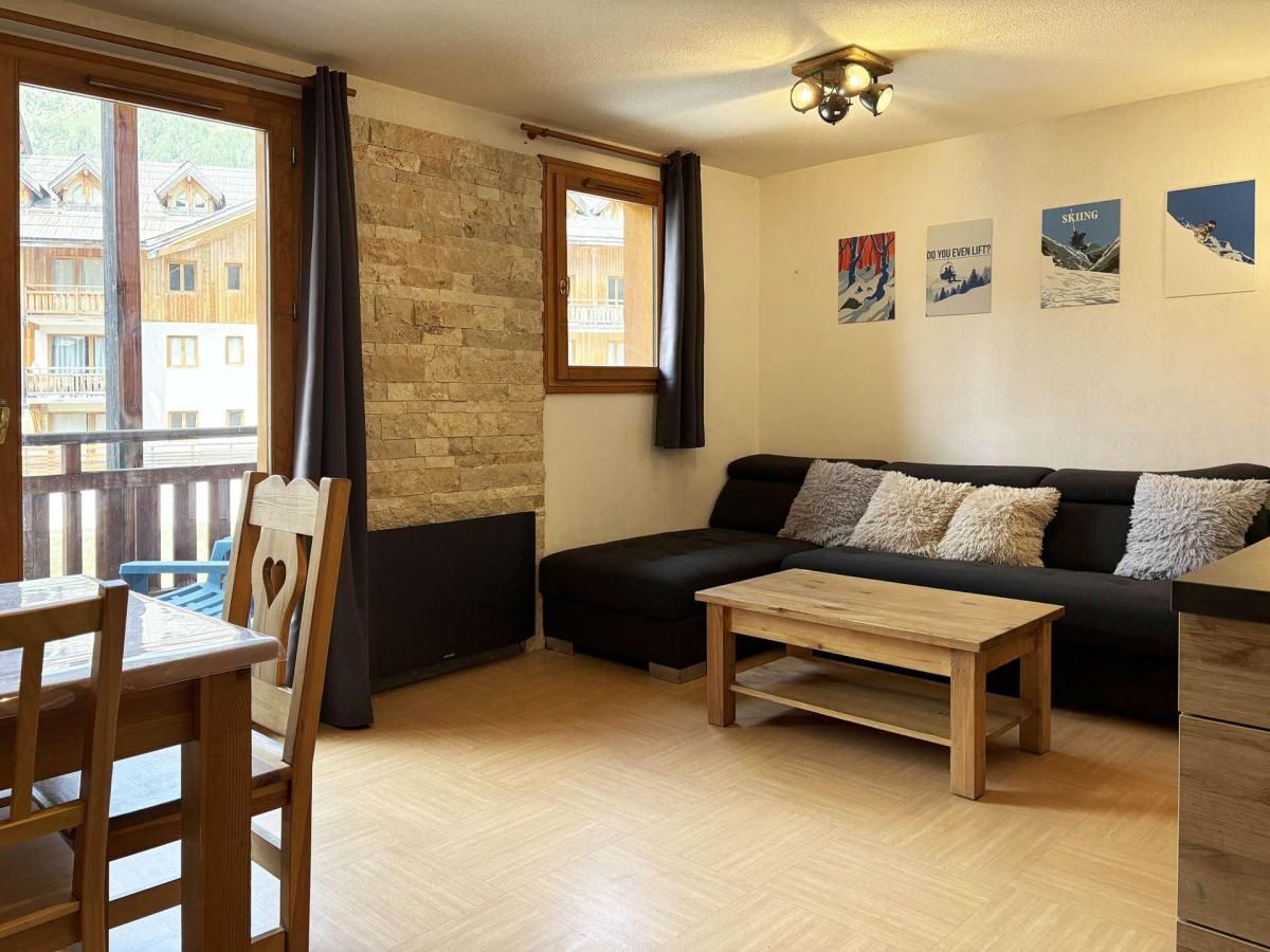 Ein Wohnzimmer mit schwarzem Sofa, Couchtisch aus Holz und Blick auf Gebäude durch ein Fenster.