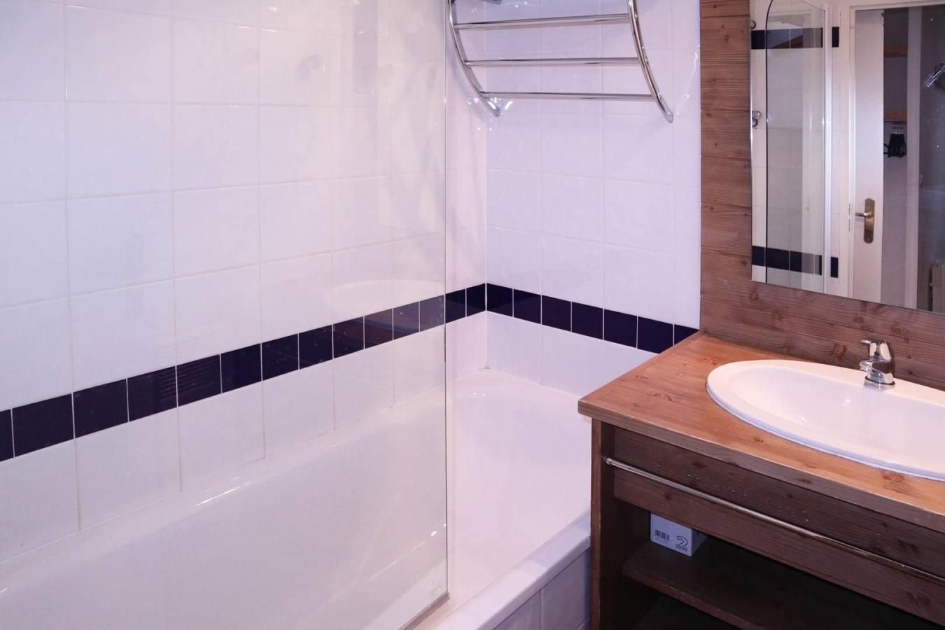 Un baño con azulejos blancos, una bañera, un tocador de madera y una cabina de ducha con paredes de cristal.