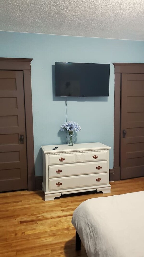 Un dormitorio con cama, cómoda con cajones, televisor de pantalla plana montado en la pared y dos puertas.