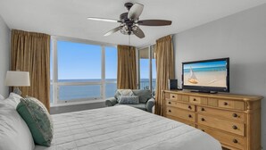 Ett hotellrum med en stor säng, en tv, en takfläkt och utsikt över havet.