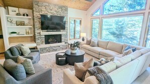 Una sala de estar moderna con chimenea de piedra, televisor de pantalla plana y ventanas amplias que ofrecen vistas al exterior.