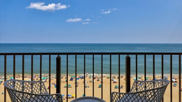 Een balkon met metalen hekwerk, met uitzicht op een strand met veel parasols en mensen.