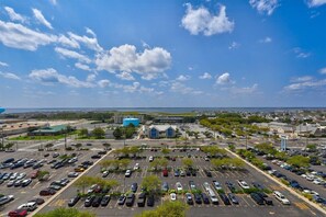 Un grand parking avec de nombreuses rangées de voitures garées et quelques bâtiments en arrière-plan.