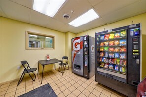 Ein Automatbereich mit einem Gatorade-Kühler und einem Snackautomaten. Zwei Stühle und ein kleiner Tisch sind vorhanden.