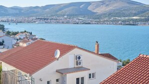 A coastal town with terracotta-roofed buildings, a body of water, and mountains in the background. - Queen's Lodge Mastrinka by Litto (Mastrinka)