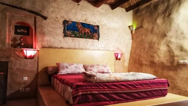 A bedroom with a bed, a headboard, a wall-mounted painting, and a wall-mounted light fixture.