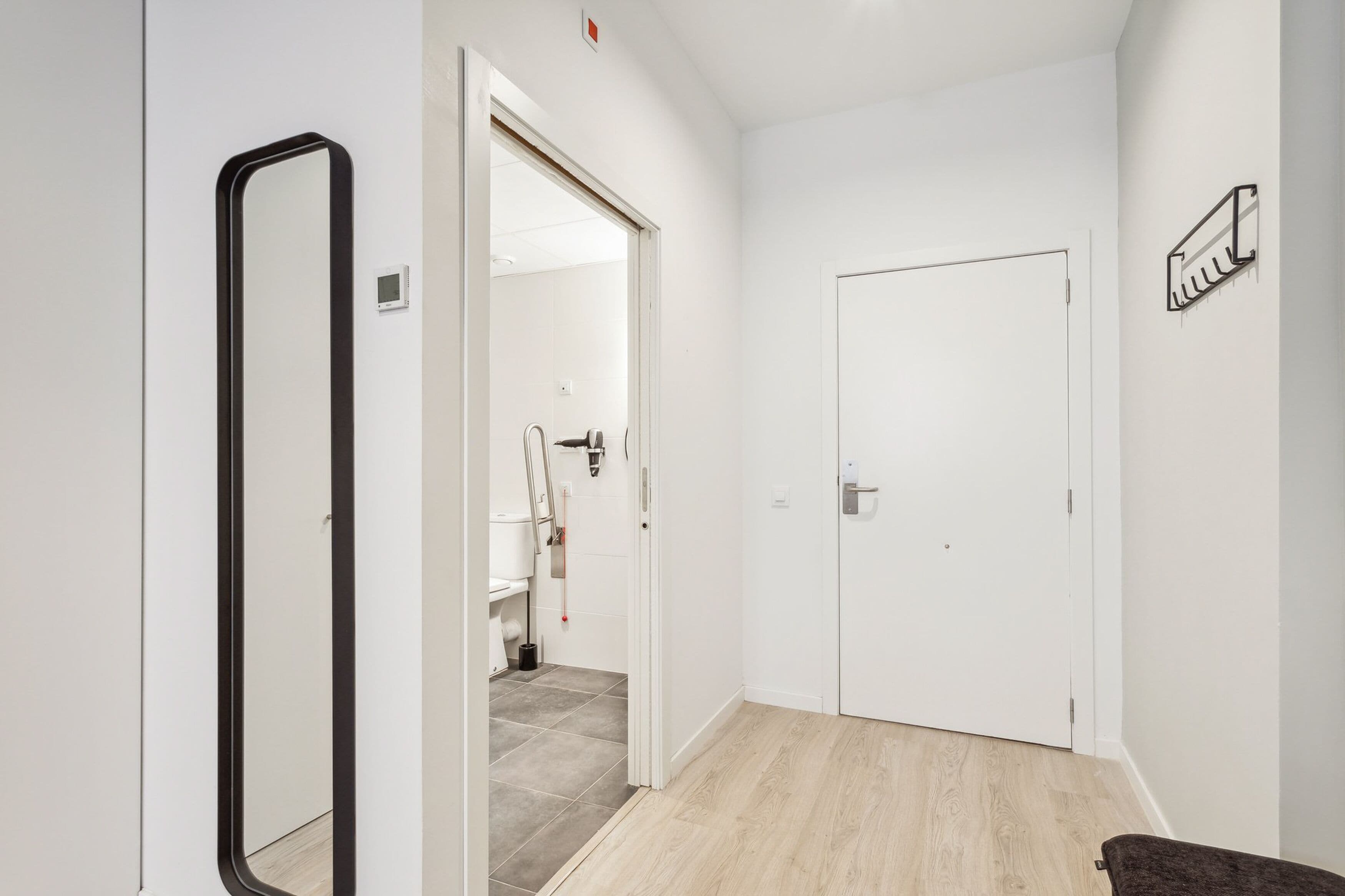 Un couloir avec une porte blanche, un miroir et un porte-serviettes.