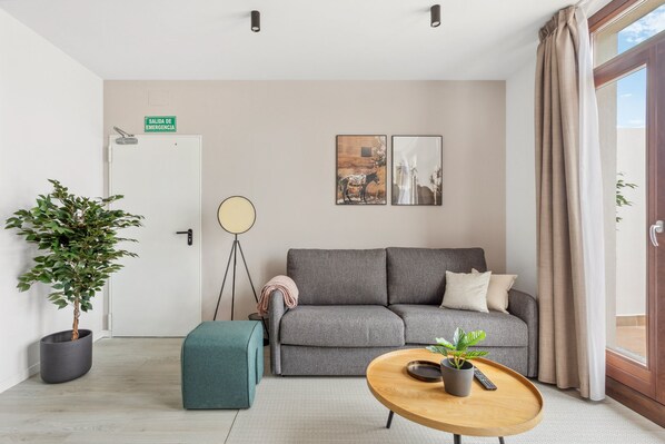 A modern living room with a grey sofa, a round coffee table, a potted plant, and a floor lamp. - Limehome Valencia Calle de Cadiz (Valencia)