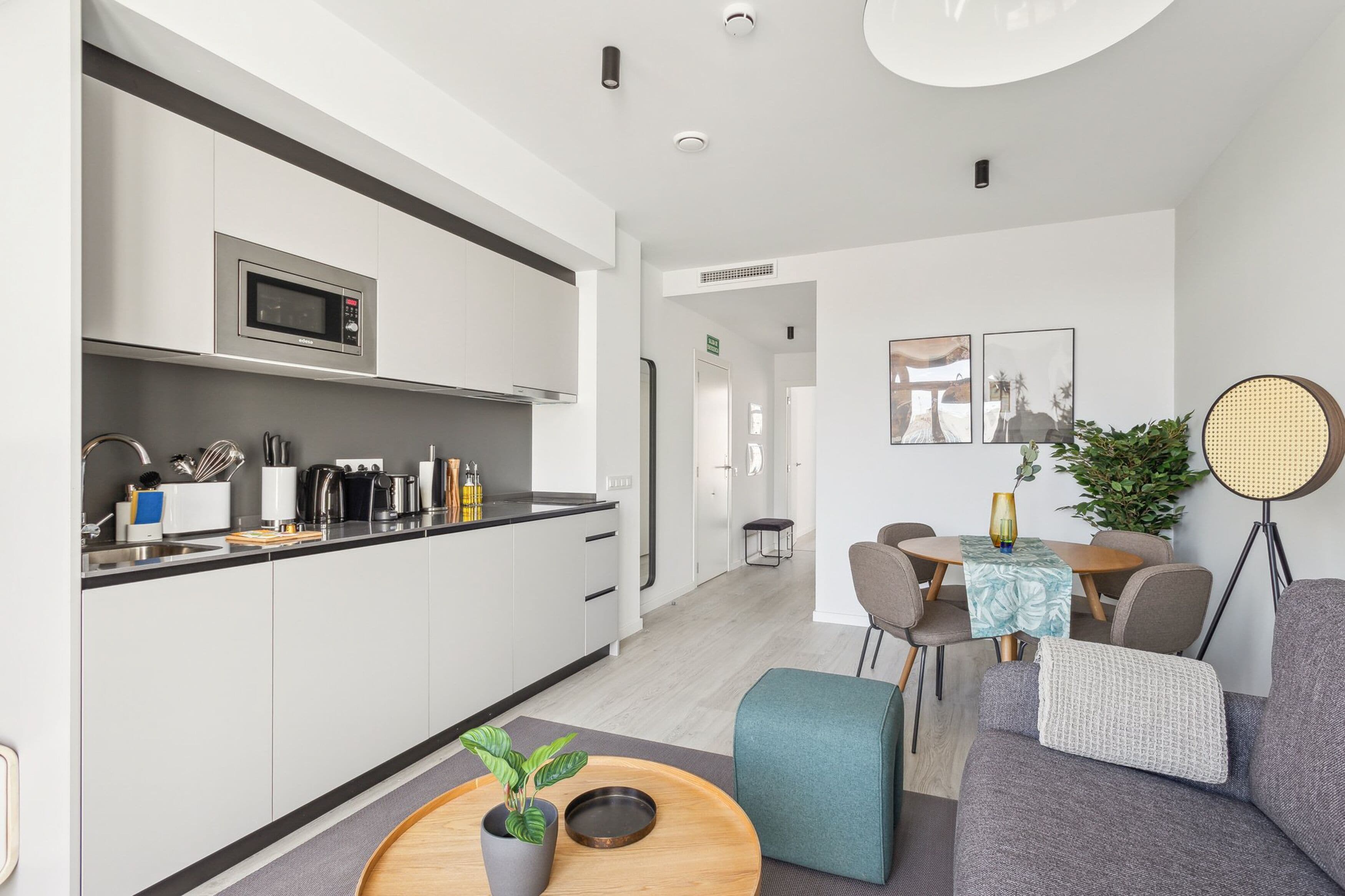 A modern kitchen with a microwave, stove, and various utensils. There is a dining area with a table and chairs, and a sofa.