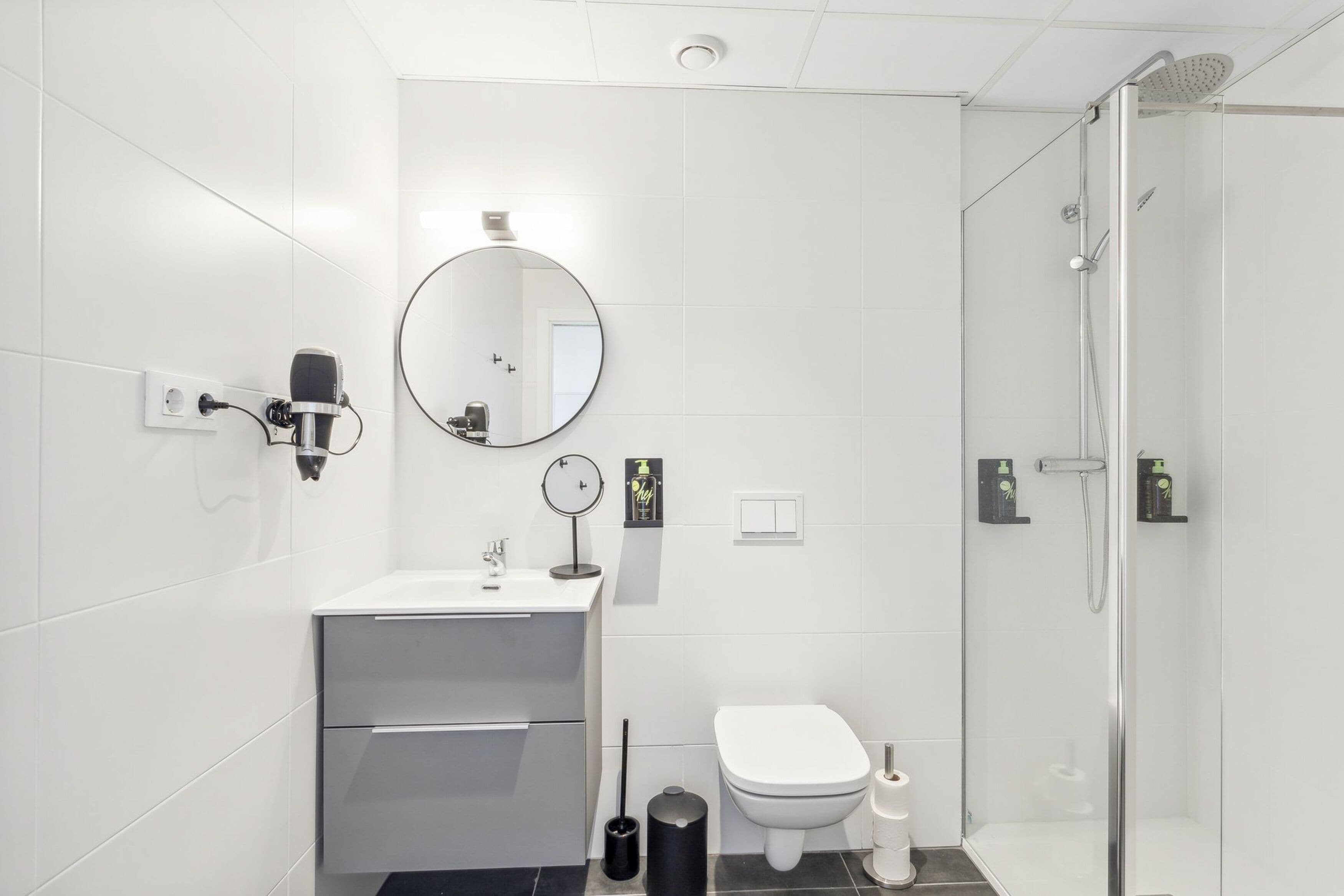 A modern bathroom with a glass shower enclosure, a round mirror, a white sink, and a toilet.