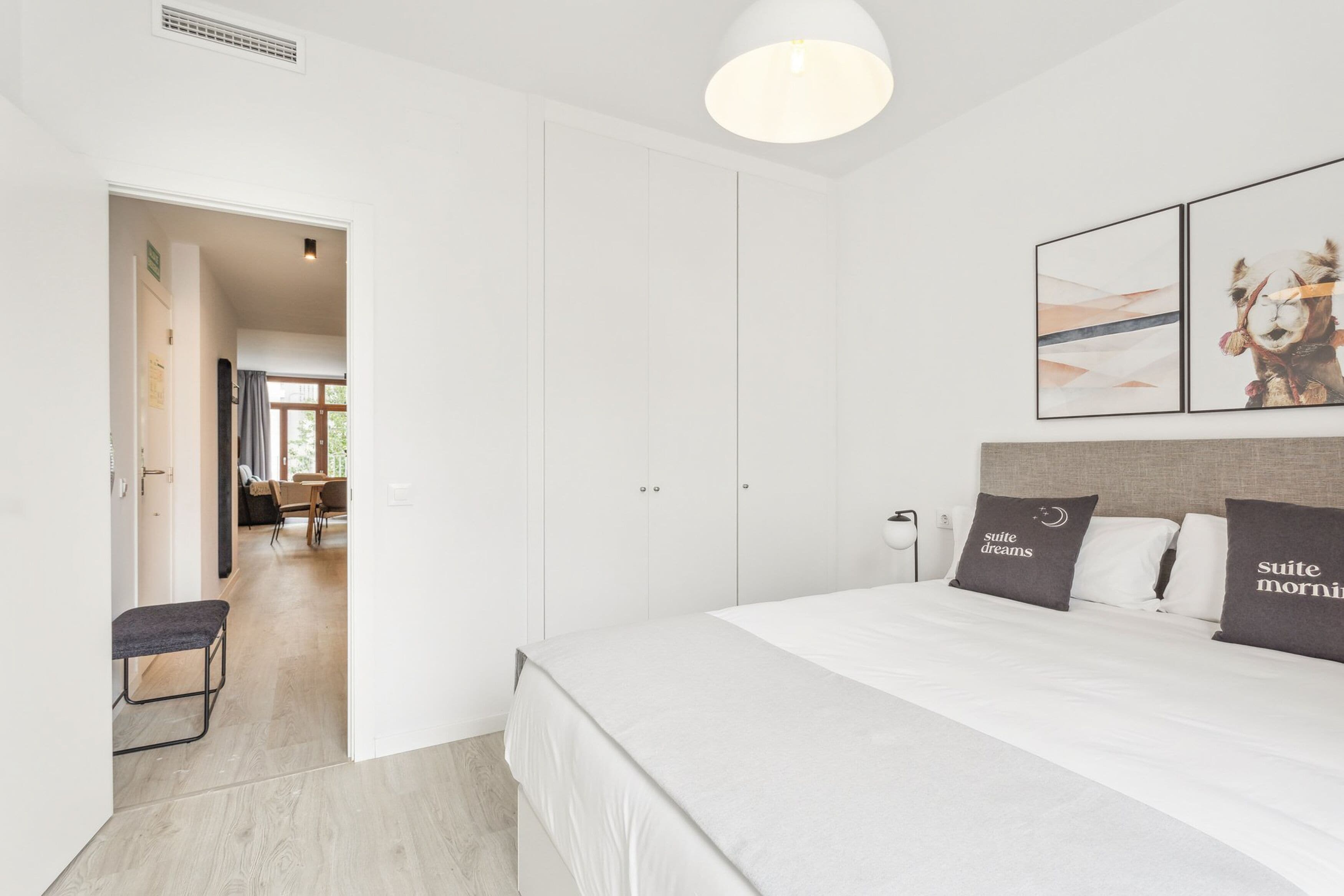 A modern bedroom with a large bed, a bench, and a view into another room.