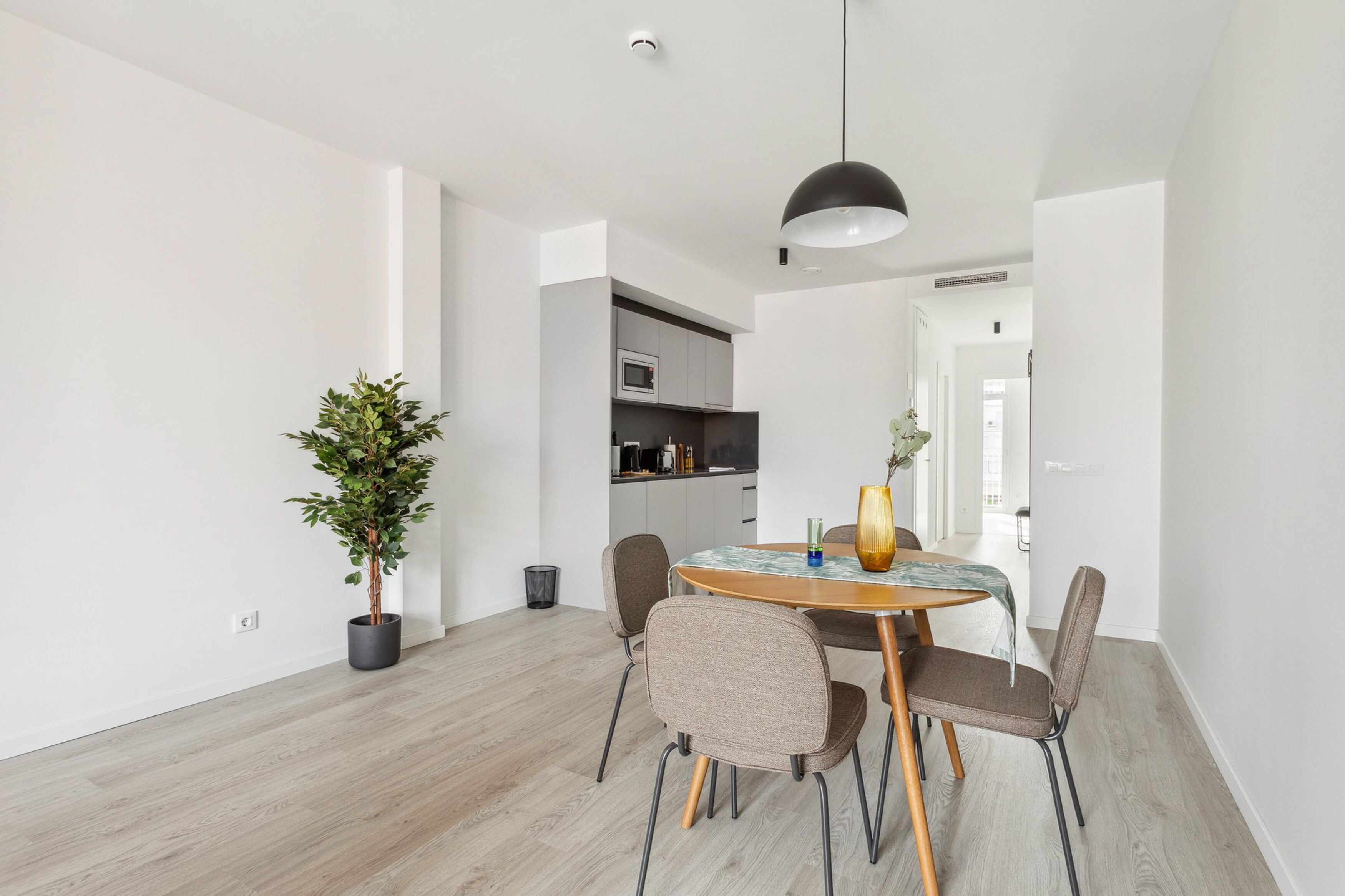 Et moderne spiseområde med et rundt bord, fire stole, en potteplante og et hængende lys.