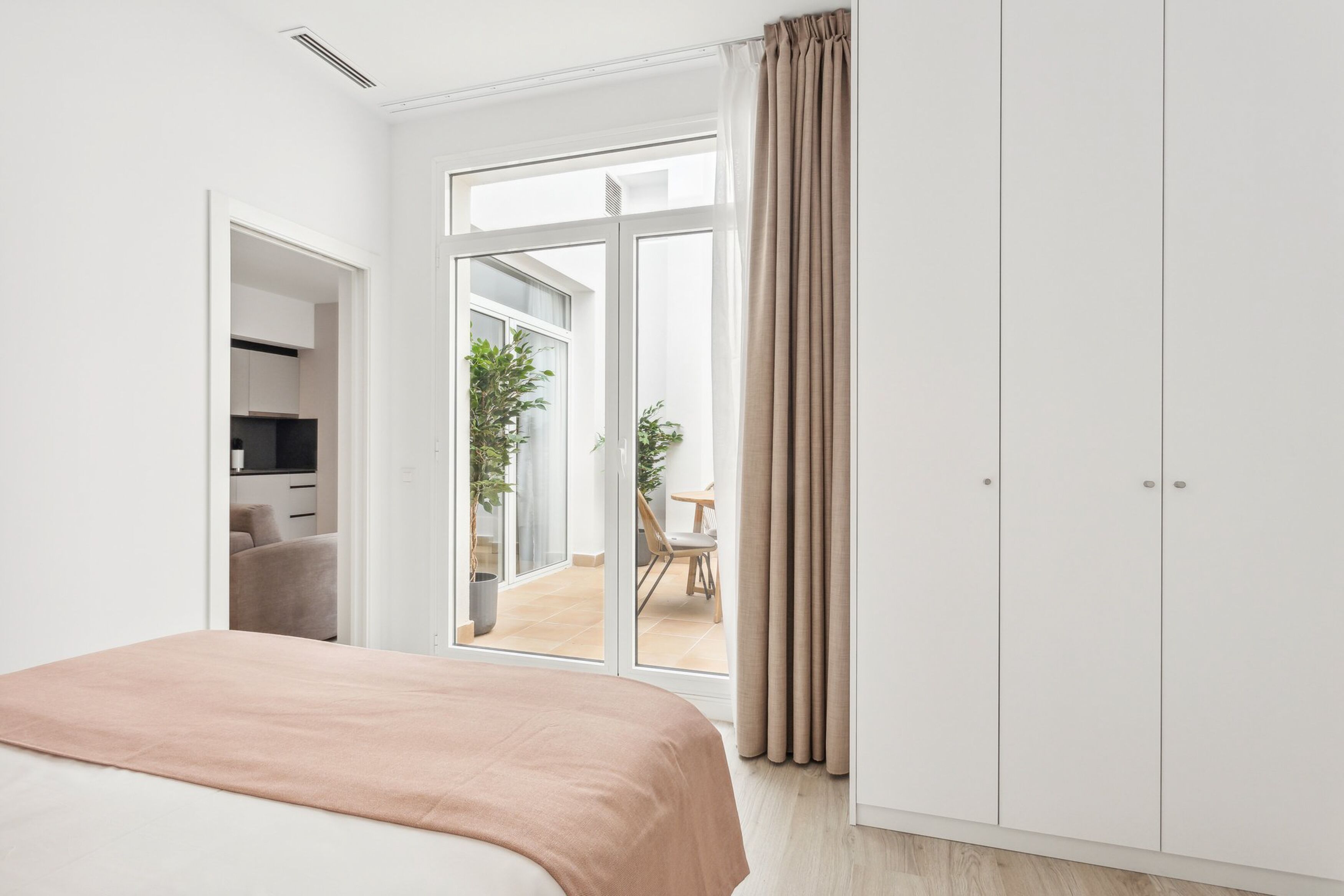 Un dormitorio moderno con una cama grande, una puerta corrediza de vidrio a un balcón y vistas al exterior.