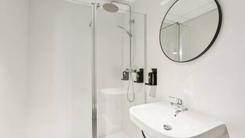 Un baño moderno con ducha envuelta en vidrio, lavamanos blanco y espejo redondo en la pared.