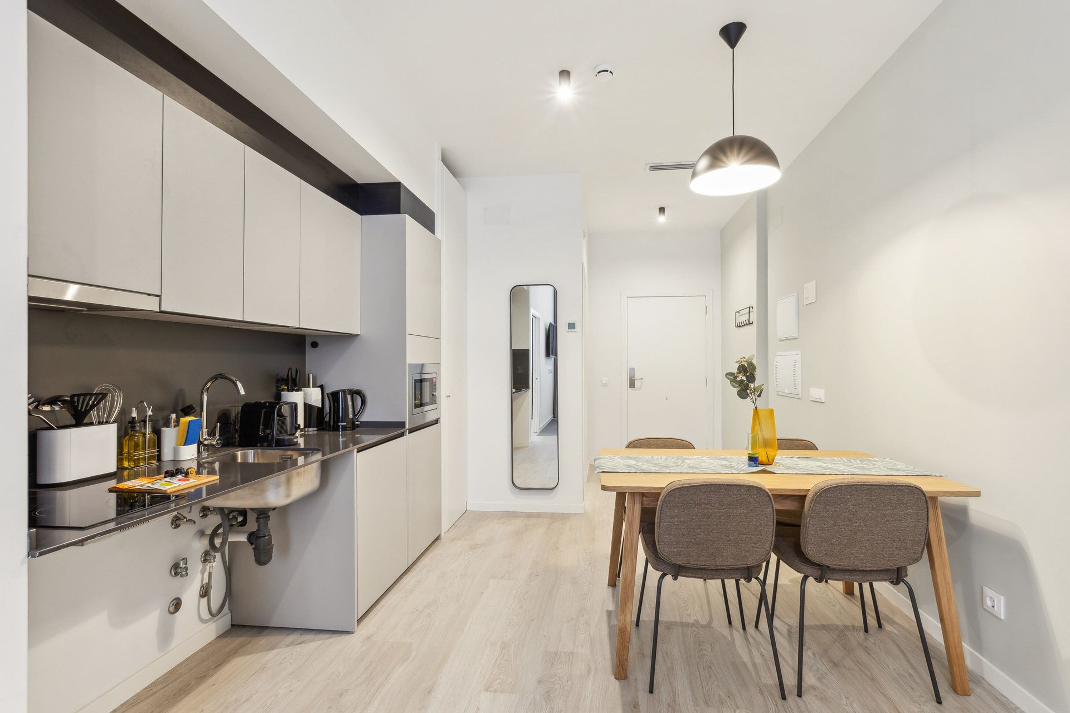 A modern kitchen with a built-in oven, a sink, and a dining area with a table and chairs.