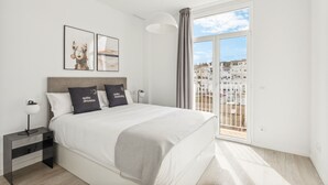 A modern bedroom with a large bed, a nightstand, and a view of a cityscape through a sliding glass door. - Limehome Valencia Calle de Cadiz (Valencia)