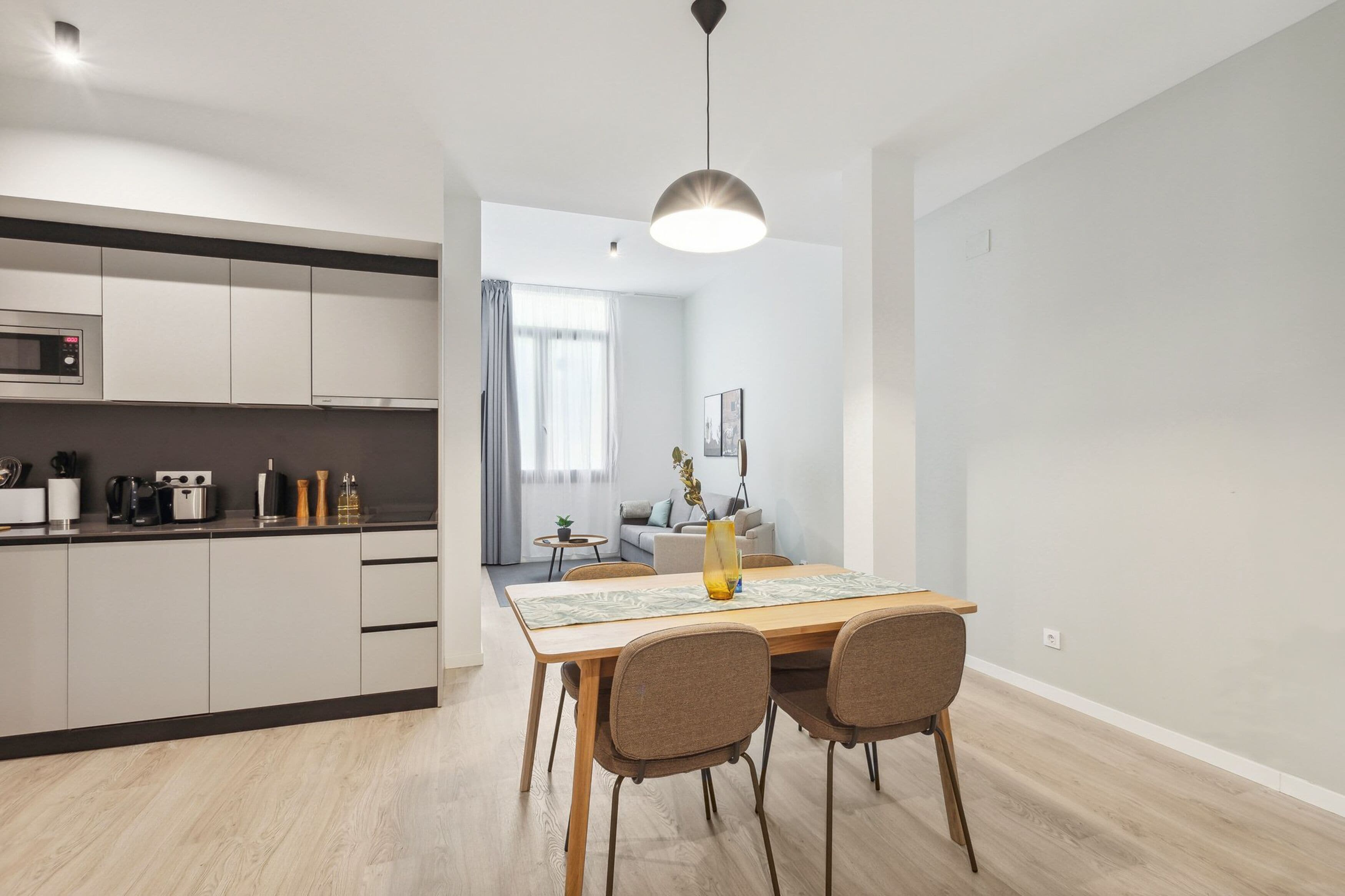 Una cocina moderna con electrodomésticos integrados y una zona de comedor con mesa y sillas de madera.