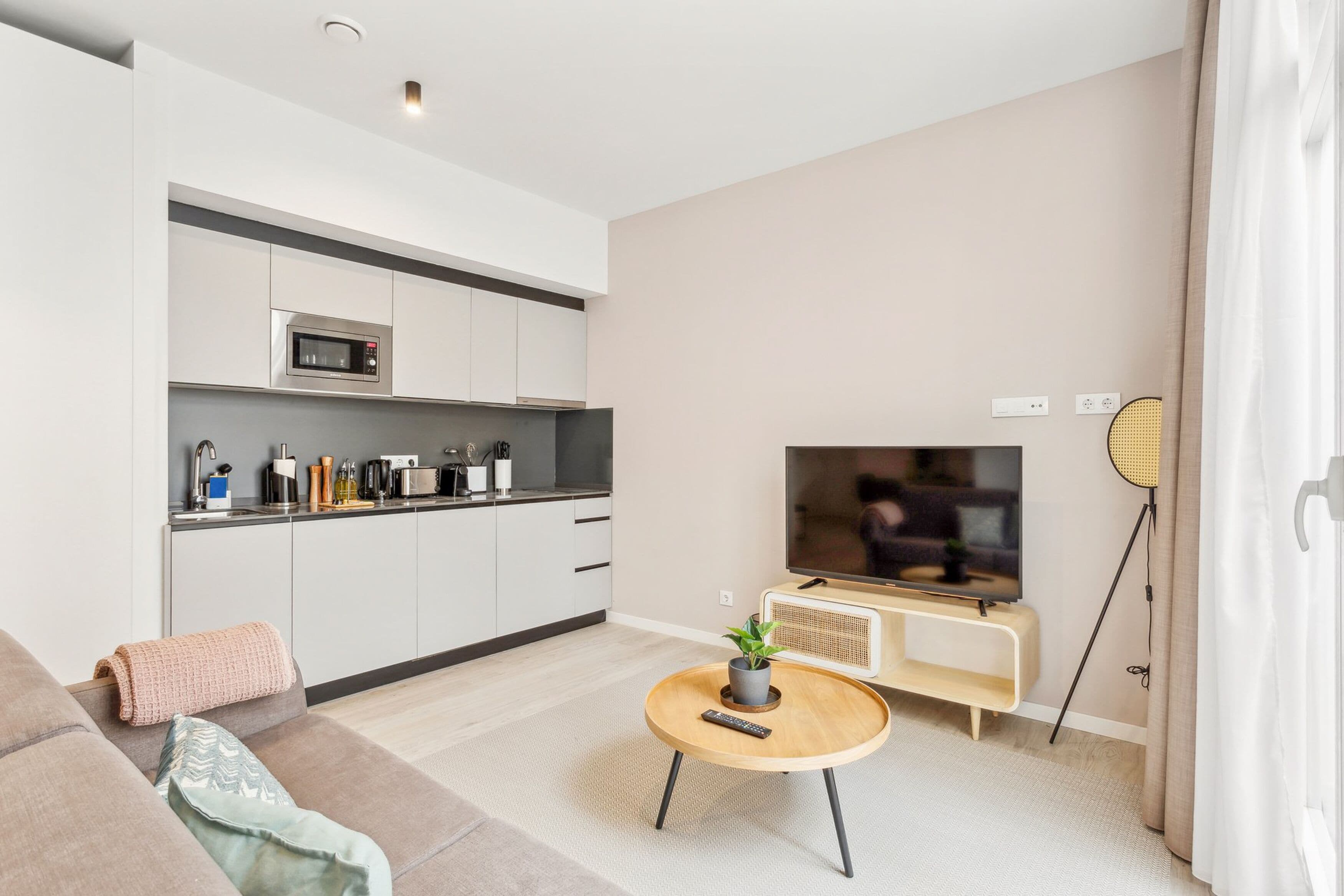 A modern living room with a sofa, a coffee table, a TV, and a kitchenette.