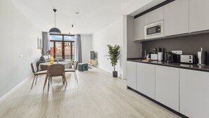A modern kitchen with grey cabinets, a microwave, and a toaster. There is a dining area with a table and chairs, and a potted plant. - Limehome Valencia Calle de Cadiz (Valencia)