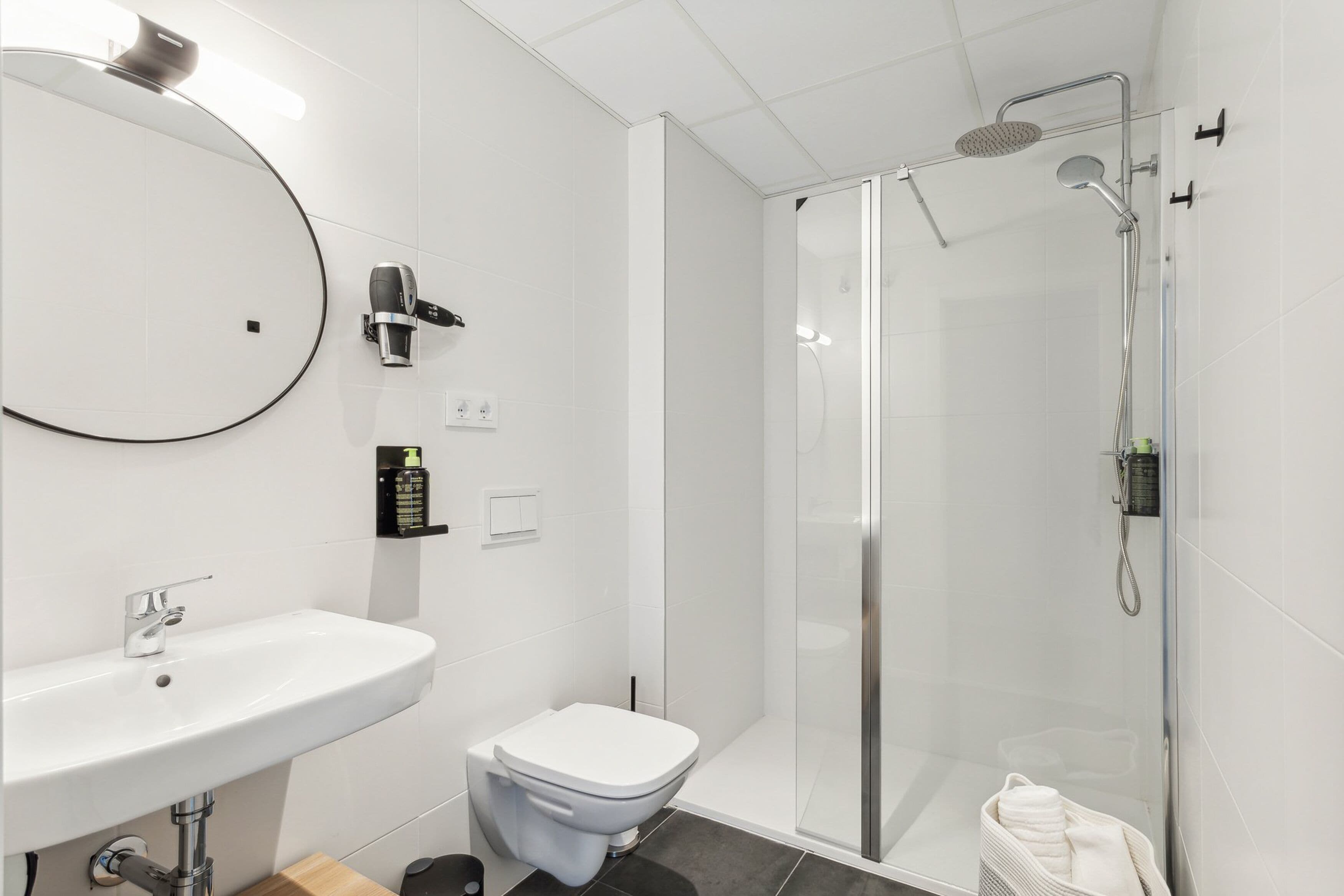Een moderne badkamer met een wit wastafel, toilet en douchecabine met glazen wanden.