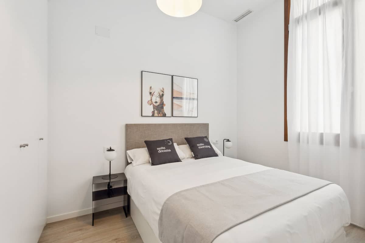 A modern bedroom with a bed, bedside tables, a nightstand, and a wall-mounted artwork.