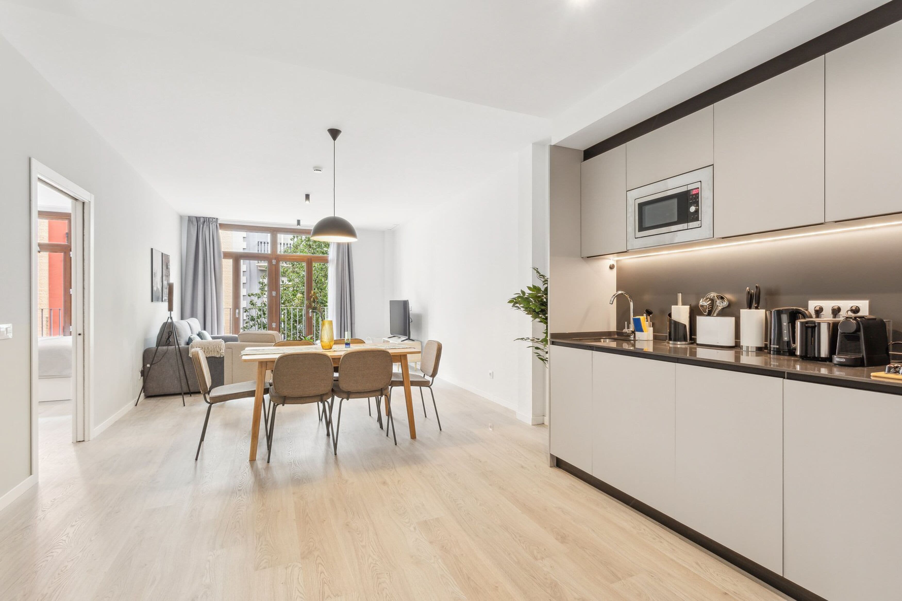 Eine moderne Küche mit integriertem Mikrowellenherd, einem Essbereich mit Tisch und Stühlen und Blick ins Freie durch große Fenster.