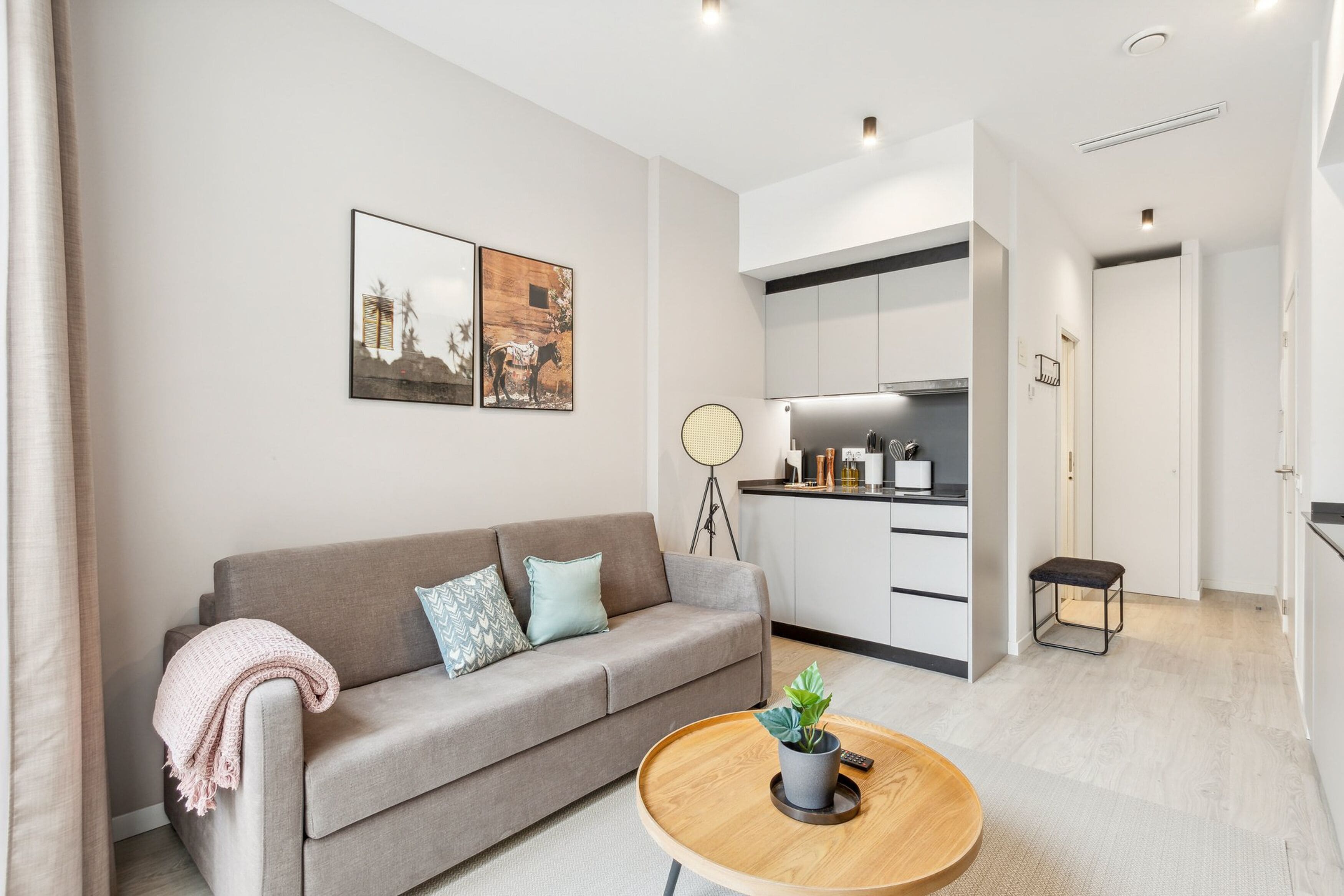 Sala de estar moderna com sofá, mesa de centro com planta e área de cozinha com armários e ventilador.