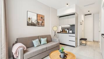 Sala de estar moderna com sofá, mesa de centro com planta e área de cozinha com armários e ventilador.