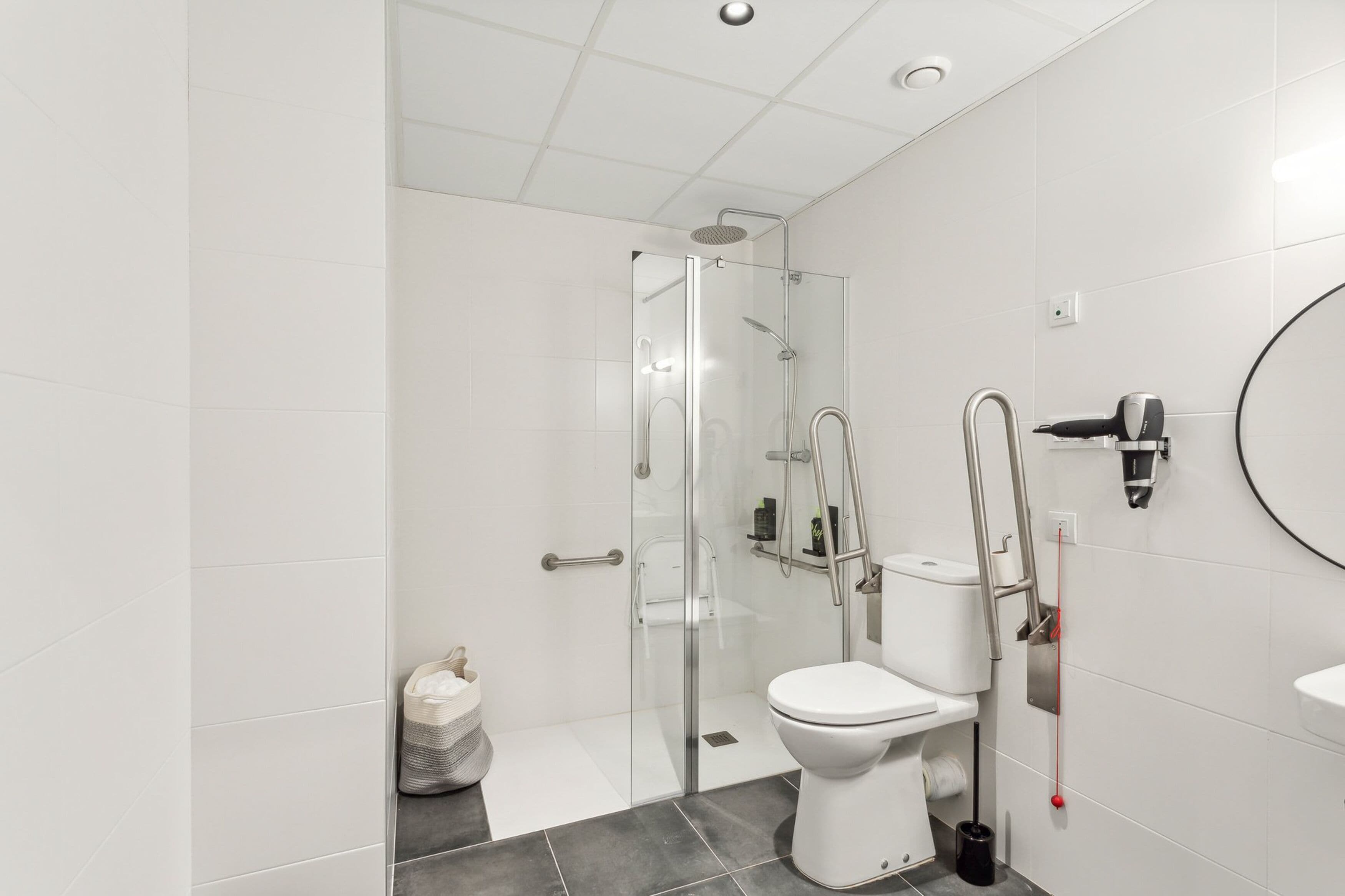 Ein modernes Badezimmer mit einer gläsernen Duschkabine, einer weißen Toilette und einem runden Spiegel.