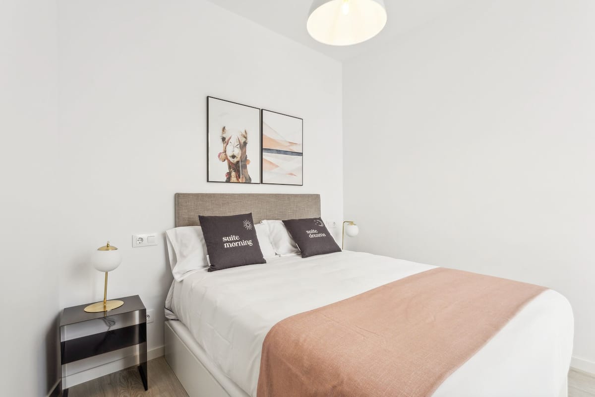 A neatly made bed with a white and brown blanket, two bedside tables with lamps, and two framed pictures on the wall.
