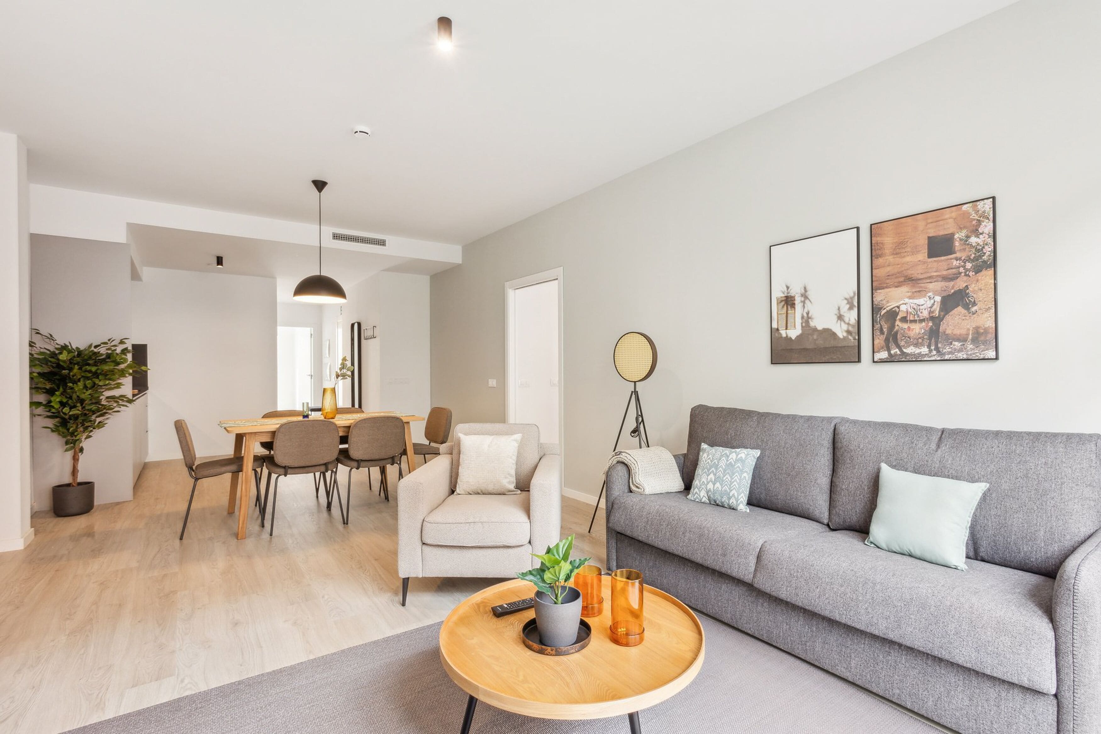 A modern living room with a grey sofa, a wooden coffee table, and a dining area with a table and chairs.