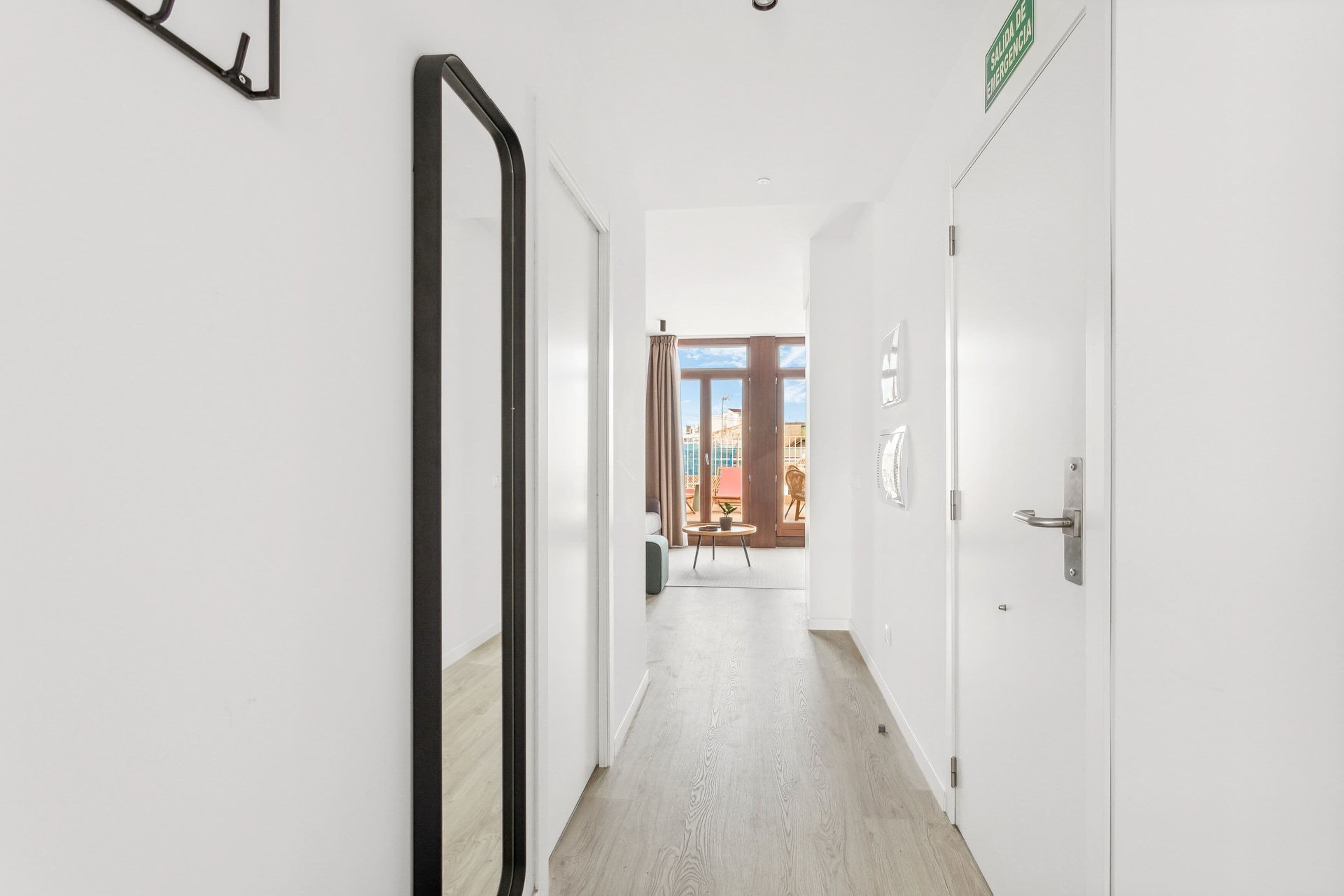A hallway with a mirror on the left, a door on the right, and a view of an outdoor seating area with a table and chairs.