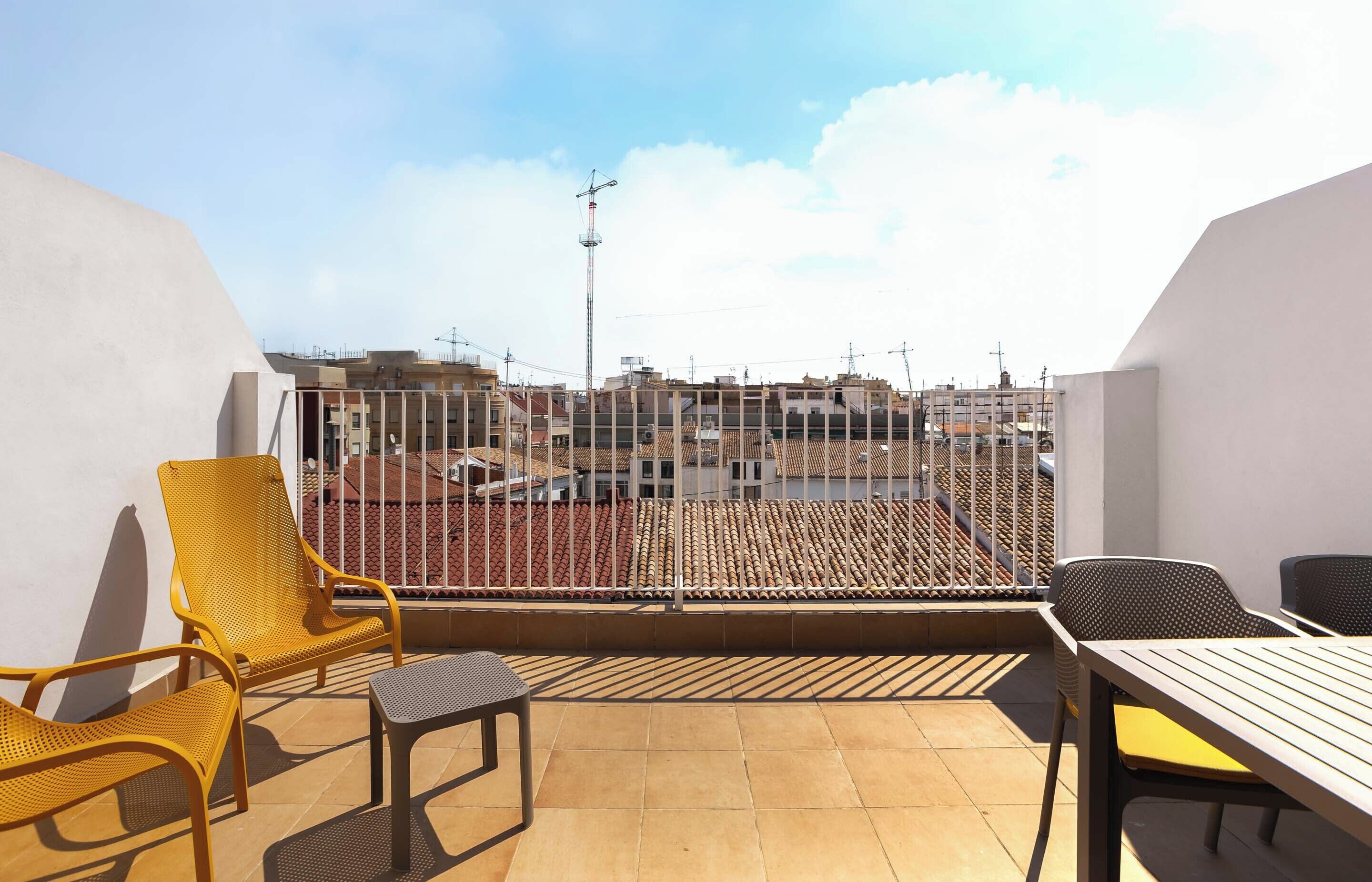 A balcony with yellow chairs and a table, overlooking a cityscape with buildings and a crane.