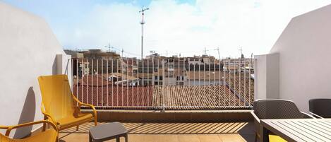 A balcony with yellow chairs and a table, overlooking a cityscape with buildings and a crane.