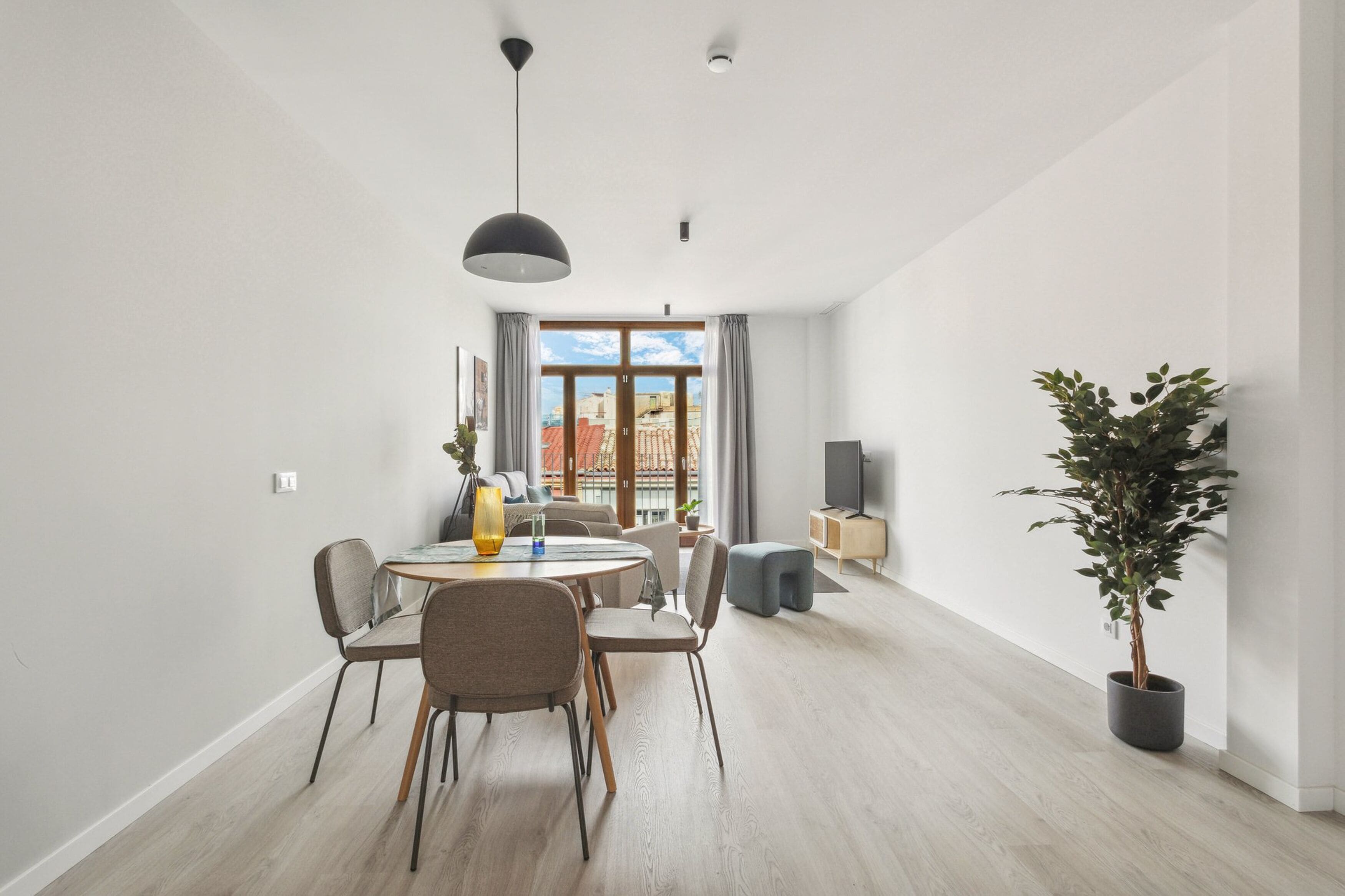 A modern living room with a dining area, large windows, and a potted plant.