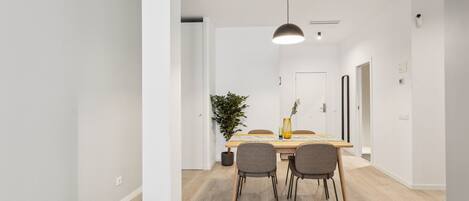 A modern dining area with a wooden table, four chairs, a potted plant, and a pendant light.