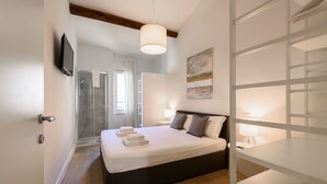 A modern bedroom with a large bed, bedside lamps, a TV, and a shower area. - Novella Contemporary Apartment by Mmega (Florence)